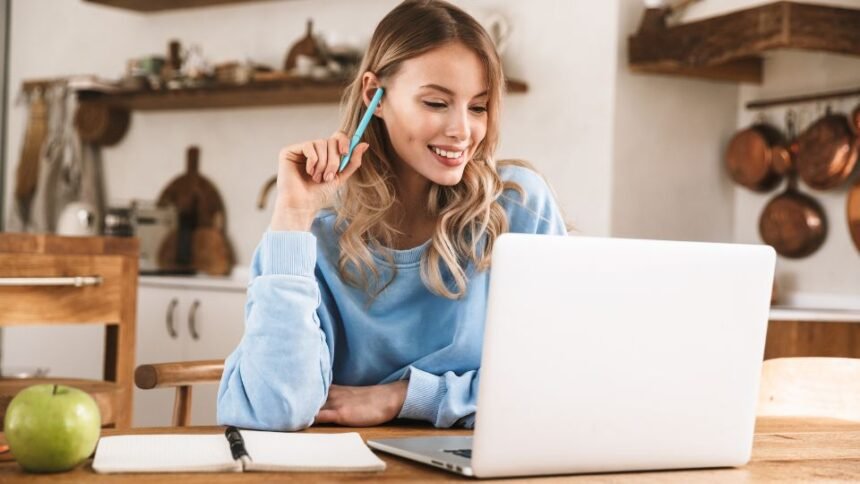 Fiatal nő otthoni irodában dolgozik laptopon, produktív környezetben.