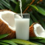 Friss kókuszvíz egy pohárban, kókuszdiók mellett, zöld levelek között.