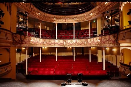 Színházi előcsarnok piros székeivel és színpaddal.