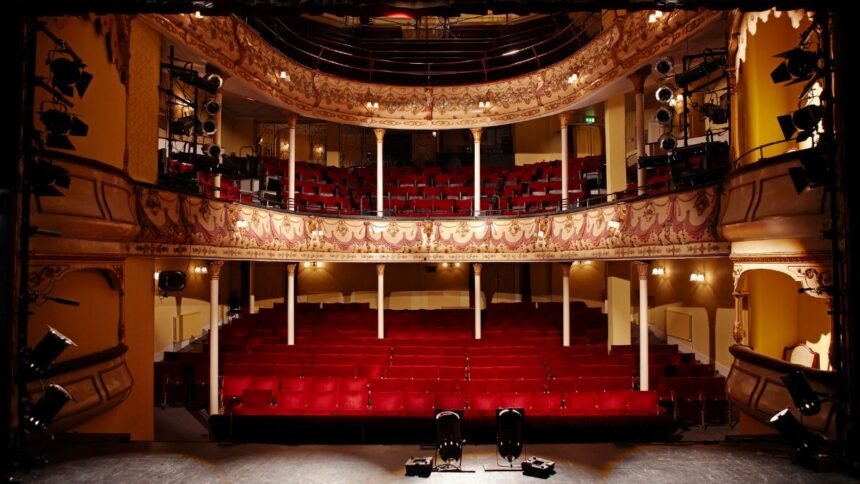 Színházi előcsarnok piros székeivel és színpaddal.