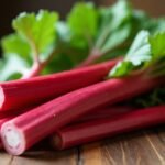 Friss rebarbara szárak zöld levelekkel, faasztalon.